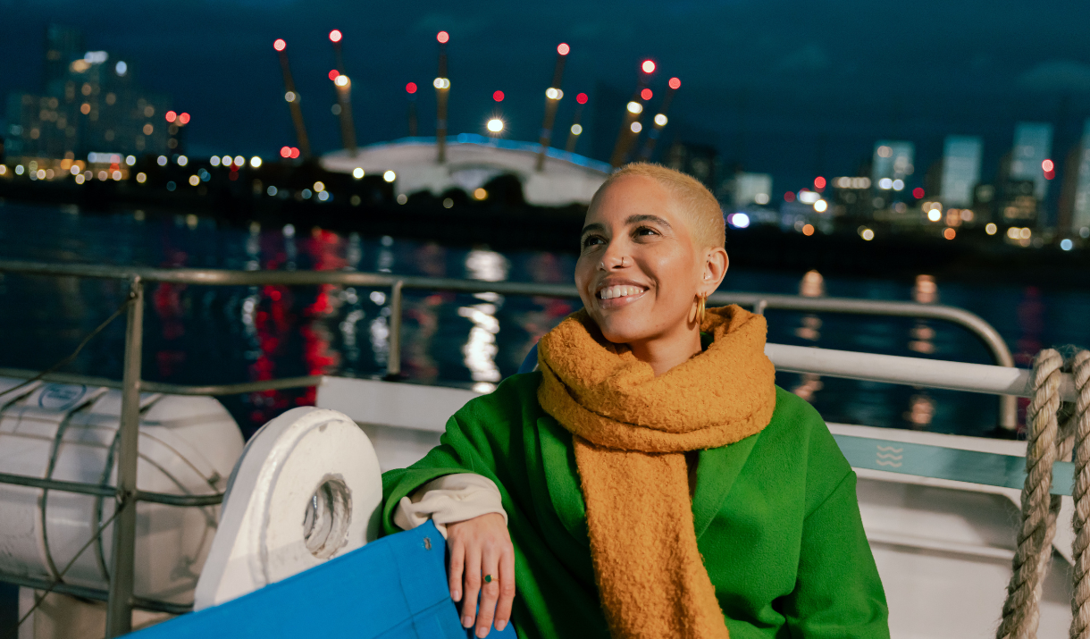 Woman on rear deck of Uber Boat by Thames Clippers in front of The O2 at night